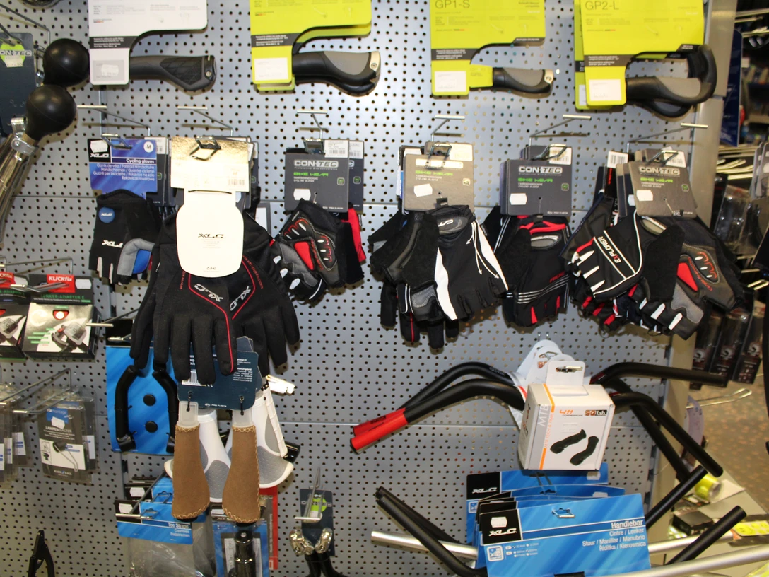 Fahrradzubehör Verschiedene Fahrradhandschuhe in vielfältigen Stilen und Größen hängen an einer perforierten Wand.