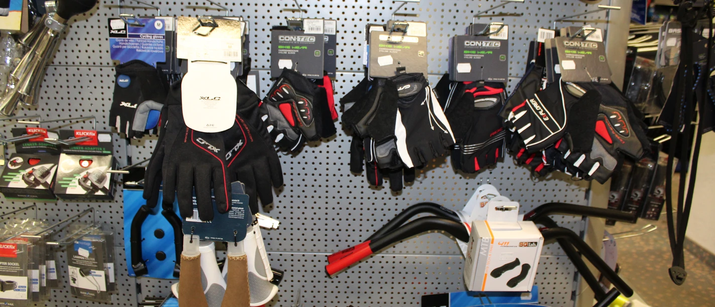 Fahrradzubehör Verschiedene Fahrradhandschuhe in vielfältigen Stilen und Größen hängen an einer perforierten Wand.