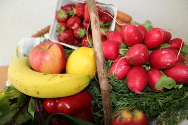 Frisches Obst und Gemüse arrangiert in einem Korb, darunter Banane, Erdbeeren, Radieschen.