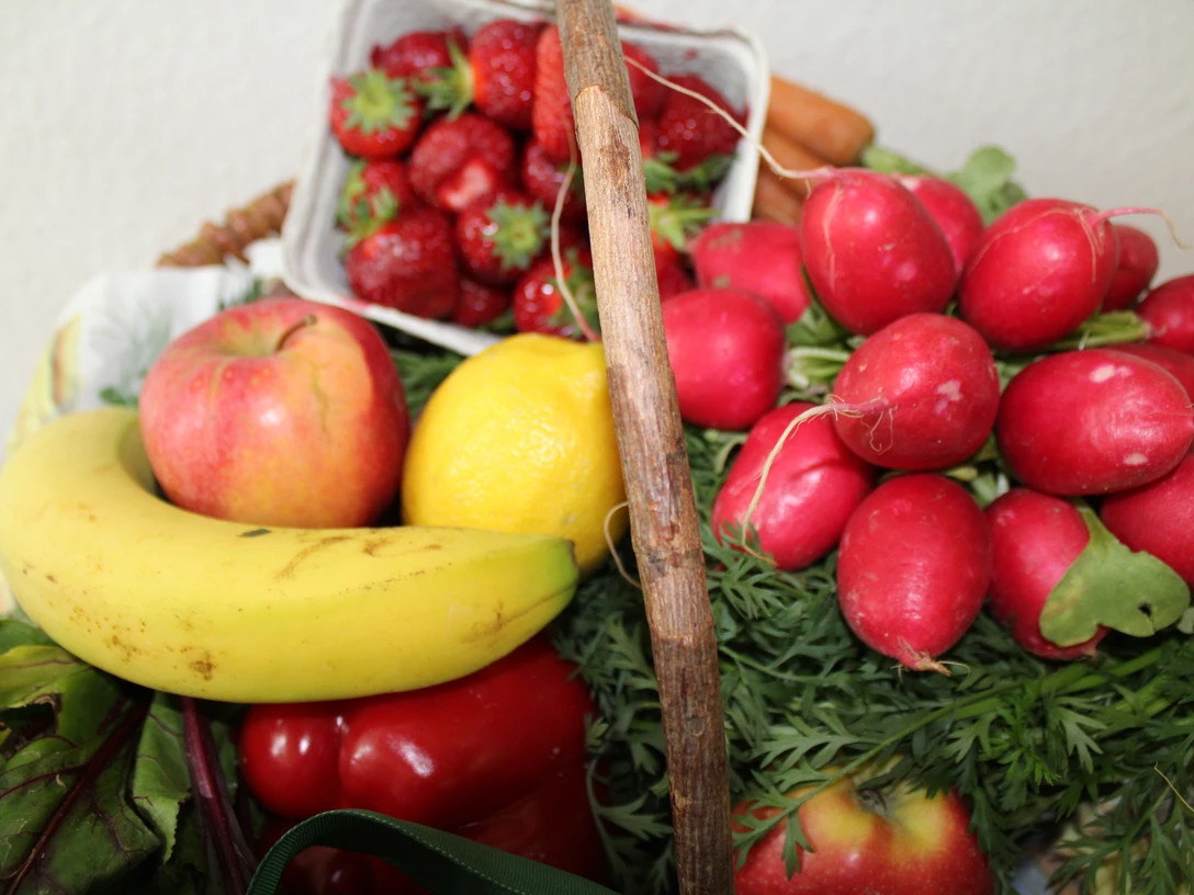 Frisches Obst und Gemüse arrangiert in einem Korb, darunter Banane, Erdbeeren, Radieschen.
