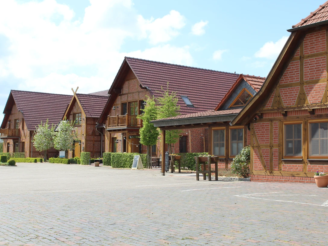 Okelmann's Historisches Hotelgebäude aus rotem Backstein mit Holzdetails, umgeben von einer gepflasterten Fläche.Historic hotel building made of red brick with wooden details, surrounded by a paved area.Historisk hotelbygning af røde mursten med trædetaljer, omgivet af et asfalteret område.Historisch hotelgebouw van rode baksteen met houten details, omgeven door een geplaveid terrein.