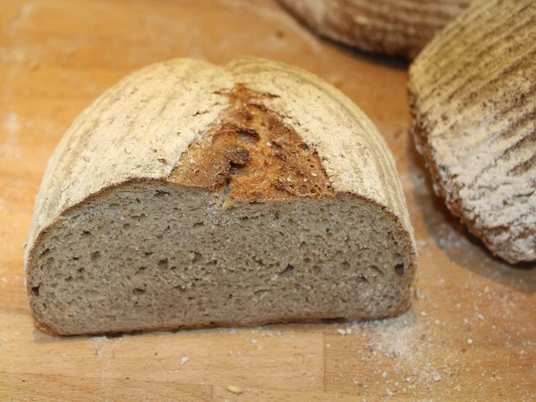 Halbiertes, krustenbetontes Brot auf einem Holzbrett mit feinem Mehl bestäubt.Halved, crusty bread on a wooden board dusted with fine flour.Halveret, sprødt brød på en træplade drysset med fint mel.Gehalveerd, knapperig brood op een houten plank bestoven met fijn meel.