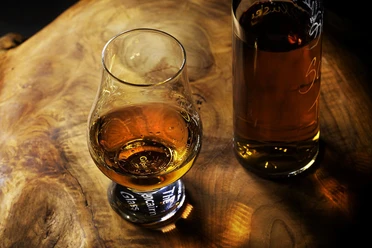 whisky-tasting Ein edles Whiskyglas und eine Flasche stehen auf einem stilvollen Holztisch, der Wärme ausstrahlt.