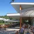 Bickbeernhof Café Menschen genießen sonnige Stunden auf der Außenterrasse eines Cafés mit modernen, weißen Sonnenschirmen.