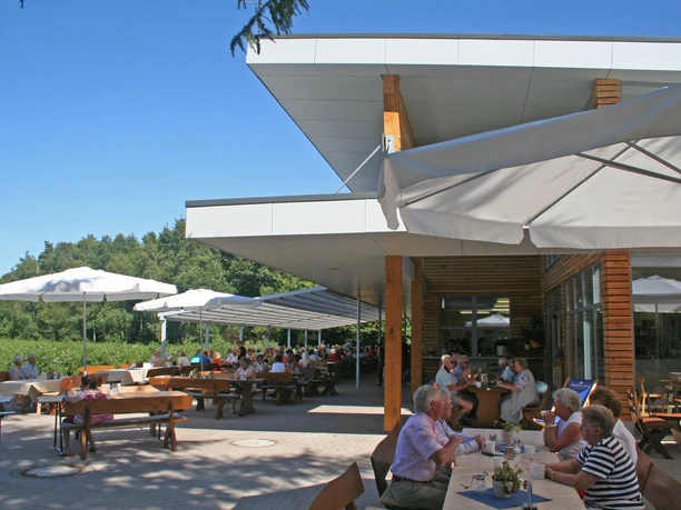 Bickbeernhof Café Menschen genießen sonnige Stunden auf der Außenterrasse eines Cafés mit modernen, weißen Sonnenschirmen.