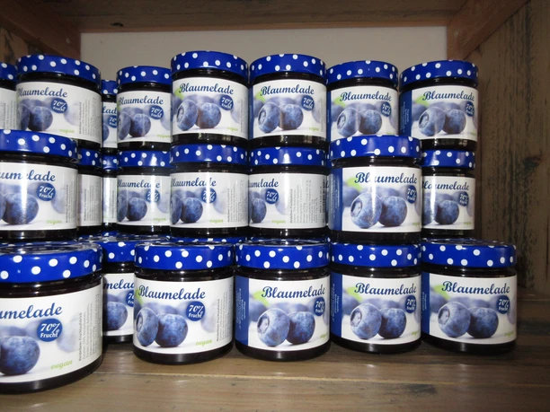 Bickbeernhof Marmelade Gläser mit Blaubeermarmelade auf einem Holzregal, verziert mit blauen Deckeln, mit 70% Fruchtanteil.