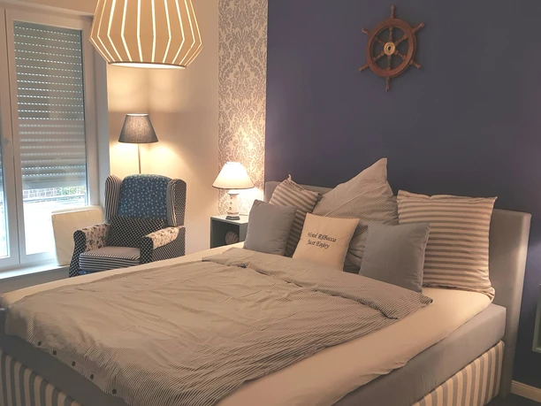 Bright and maritime bedroom with large bed, patterned wallpaper and ship-themed decoration.