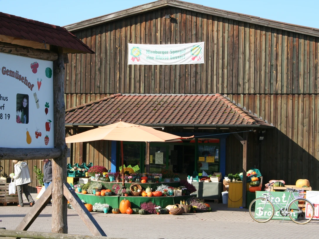 Hofladen Holthus bietet frisches Gemüse und Blumen vor einem rustikalen Holzgebäude mit Schildern.