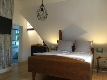 Sudweyher Bahnhof Dachzimmer mit modernem Doppelbett, Holzakzenten, Flachbildfernseher, und Zugang zum hellen Bad.