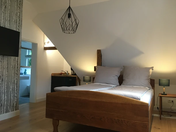 Sudweyher Bahnhof Dachzimmer mit modernem Doppelbett, Holzakzenten, Flachbildfernseher, und Zugang zum hellen Bad.