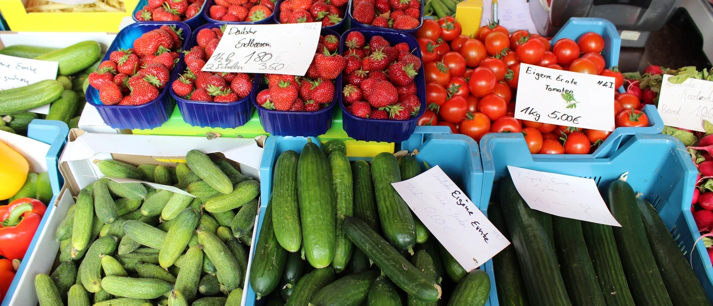 Eine bunte Auswahl frischer Gurken, Tomaten und Erdbeeren, ordentlich auf einem Markt präsentiert.