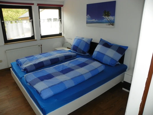 Fewo Ruth Fangmann Zwei Einzelbetten in einem hellen Raum, dekoriert mit blau-karierter Bettwäsche und Fenster im Hintergrund.