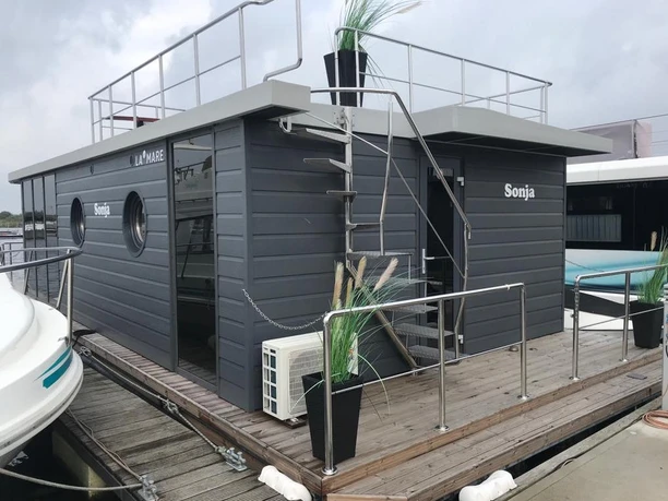 La Mare Apartboat Schwimmendes Hausboot namens "La Mare" mit Deck und Pflanzen in einem kleinen Hafen angelegt.