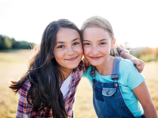 Portrait of two school children standing on field trip in nature, looking at camera.