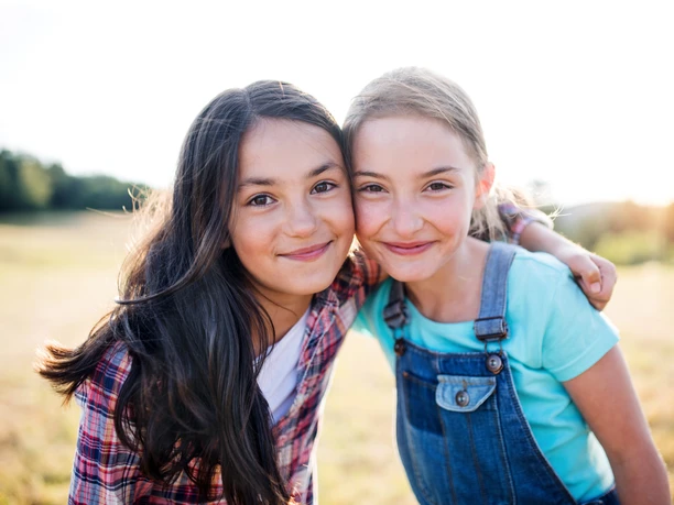 Portrait of two school children standing on field trip in nature, looking at camera.