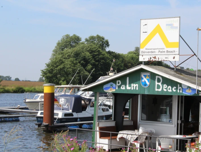 Am Ufer des Wassersportvereins Palm Beach Dörverden liegen Boote vor der mit Flaggen dekorierten Hütte.