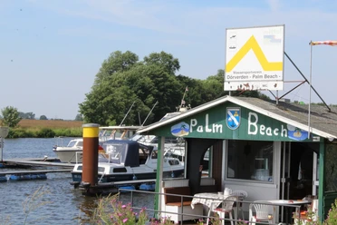Wassersportverein Palm Beach Dörverden Am Ufer des Wassersportvereins Palm Beach Dörverden liegen Boote vor der mit Flaggen dekorierten Hütte.