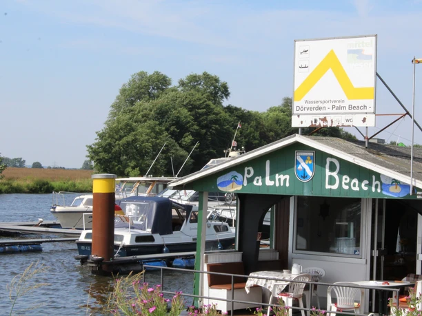 Wassersportverein Palm Beach Dörverden Am Ufer des Wassersportvereins Palm Beach Dörverden liegen Boote vor der mit Flaggen dekorierten Hütte.