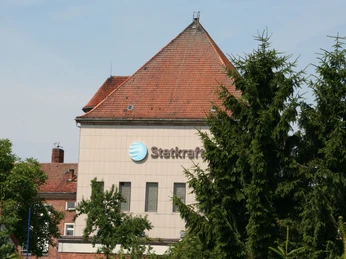 Das Statkraftwerk Dörverden mit rotem Ziegeldach eingebettet zwischen grünen Bäumen im Vordergrund.