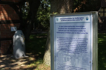 Dörverden Kalibergbau Hülsen Informationstafel zum Kalibergbau in Hülsen, umgeben von Bäumen und einem Ziegelgebäude im Hintergrund.