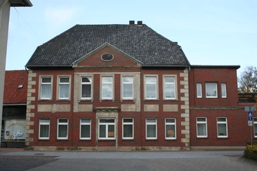 Historisches Backsteingebäude mit symmetrischer Fassade, zehn Fenstern und einem Eingang auf Kiesweg.