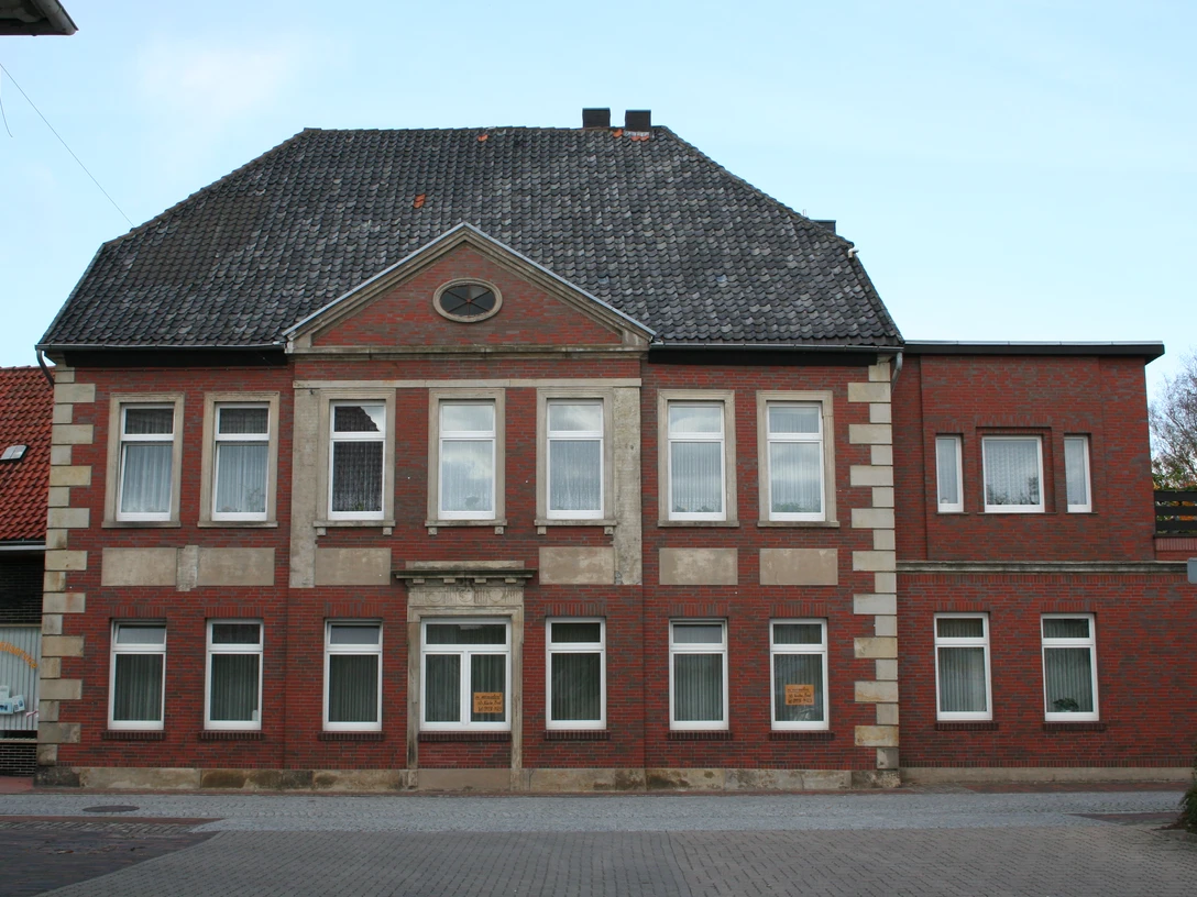 Historisches Backsteingebäude mit symmetrischer Fassade, zehn Fenstern und einem Eingang auf Kiesweg.