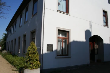 Mohrhoff-Haus Mohrhoff-Haus: Ein zweigeschossiges, weißes Gebäude mit dunklen Fenstern unter klarem Himmel.