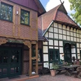 Hof Frien Fachwerkhaus mit roten Dachziegeln, grünumrahmten Fenstern und Restaurant-Schriftzug, umgeben von Bäumen.Half-timbered house with red roof tiles, green-framed windows and restaurant lettering, surrounded by trees.Bindingsværkshus med røde tagsten, vinduer med grønne rammer og restaurantbogstaver, omgivet af træer.Vakwerkhuis met rode dakpannen, ramen met groene kozijnen en restaurantbelettering, omringd door bomen.