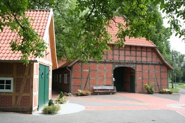 Vogelers Haus Fachwerkhaus mit rotem Ziegeldach und grünen Türen, umgeben von Bäumen, Pflaster und Bank.