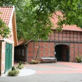 Vogelers Haus Fachwerkhaus mit rotem Ziegeldach und grünen Türen, umgeben von Bäumen, Pflaster und Bank.