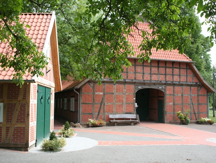 Vogelers Haus Fachwerkhaus mit rotem Ziegeldach und grünen Türen, umgeben von Bäumen, Pflaster und Bank.