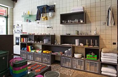 Utensil In einem hochwertig gestalteten Interieurgeschäft sind Regale an der gefliesten Wand befestigt. Verschiedenste bunte Haushaltsutensilien, Handtücher und dekorative Körbe sind in den Regalen und auf einem Holzschrank arrangiert.