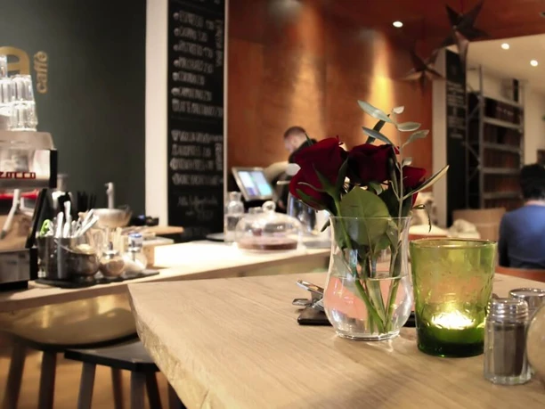 moxxa cafe die rösterei An elegant café interior with wooden counters adorned with red roses in glass vases, while candlelight creates a cosy atmosphere. A coffee bar can be seen in the background.