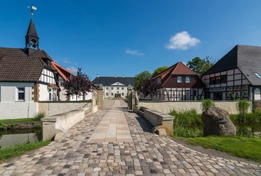 Weitblick auf Schloss Benkhausen Blick über eine gepflasterte Brücke auf Schloss Benkhausen und umgebende Fachwerkgebäude.