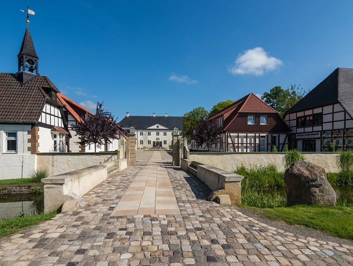 Weitblick auf Schloss Benkhausen Blick über eine gepflasterte Brücke auf Schloss Benkhausen und umgebende Fachwerkgebäude.