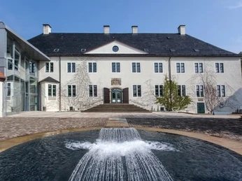 Außenansicht Modern renoviertes Gebäude mit großen Fenstern, klassischer Architektur und einem plätschernden Brunnen im Vordergrund.