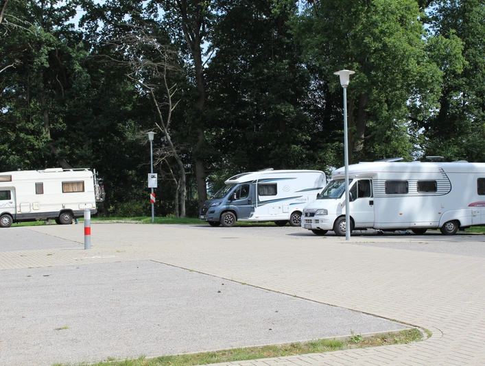 Wohnmobilstellplatz Steimbke Drei Wohnmobile parken auf einem gepflasterten Platz umgeben von hohen Bäumen bei Tageslicht.