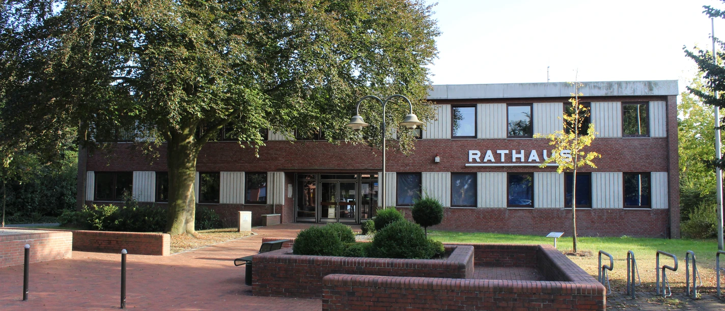 Der rote Backsteinbau des Rathauses Dörverden steht hinter grünen Bäumen und gepflegten Beeten.