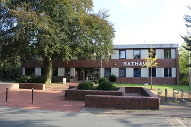 Rathaus Dörverden Der rote Backsteinbau des Rathauses Dörverden steht hinter grünen Bäumen und gepflegten Beeten.