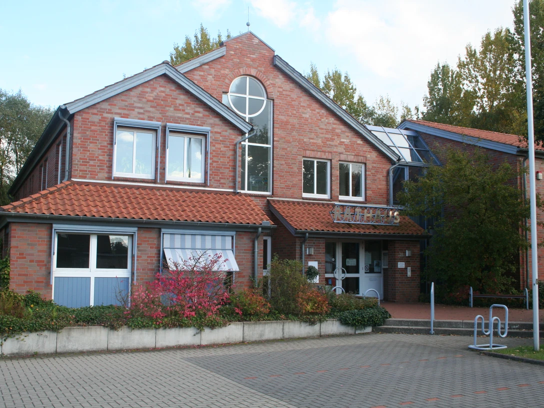 Rathaus Marklohe Rotes Backsteinrathaus mit Giebeldach, runden Fenstern und Eingangsbereich, umgeben von Bäumen.