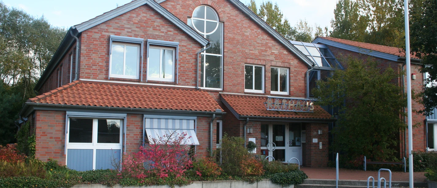 Rathaus Marklohe Rotes Backsteinrathaus mit Giebeldach, runden Fenstern und Eingangsbereich, umgeben von Bäumen.