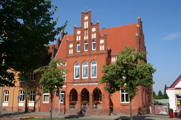 Rathaus Stolzenau Rotes Backsteingebäude mit markantem Stufengiebel, umgeben von Bäumen und blauem Himmel.