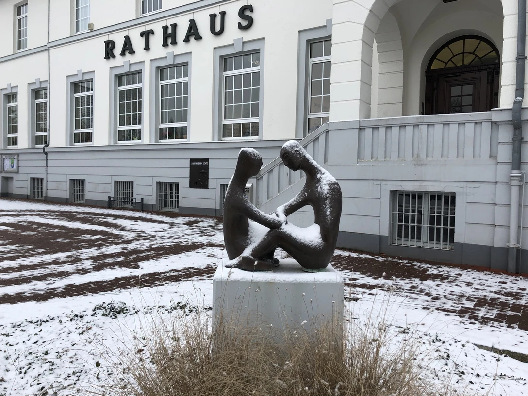 Rathaus Uchte Zwei bronzene Figuren sitzen schneebedeckt auf einem Sockel vor dem historischen Rathaus Uchte.