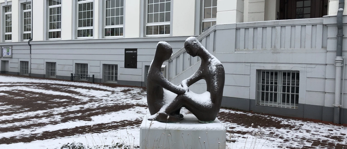 Rathaus Uchte Zwei bronzene Figuren sitzen schneebedeckt auf einem Sockel vor dem historischen Rathaus Uchte.
