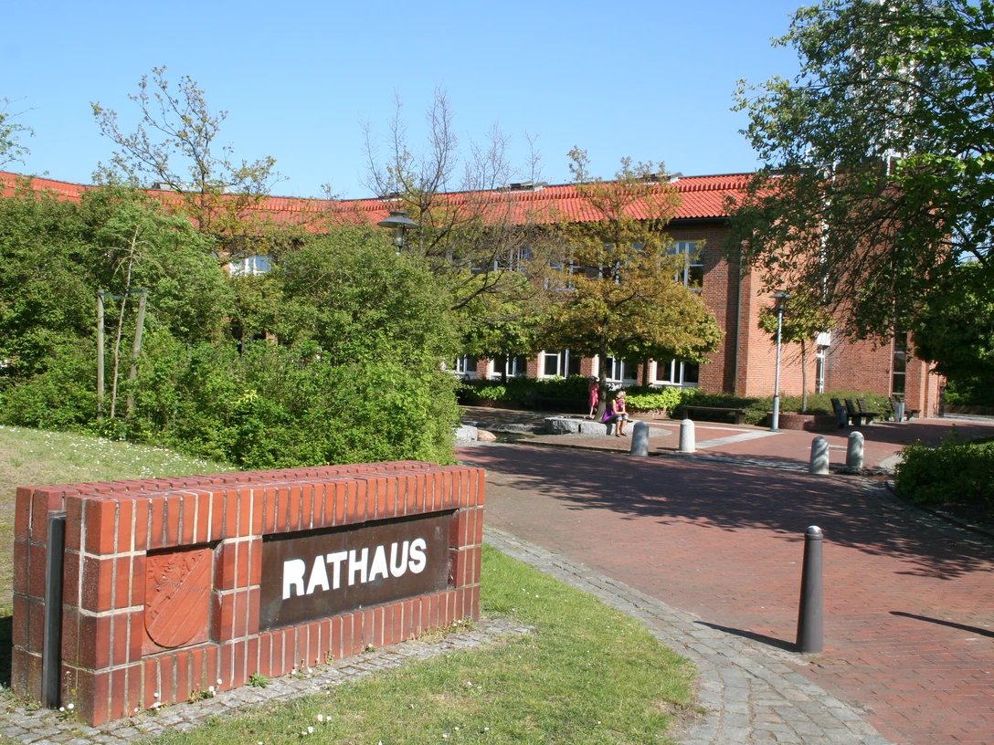 Rathaus Weyhe Backsteinbau des Rathauses Weyhe mit rotem Dach, umgeben von grünen Bäumen und blühenden Sträuchern.