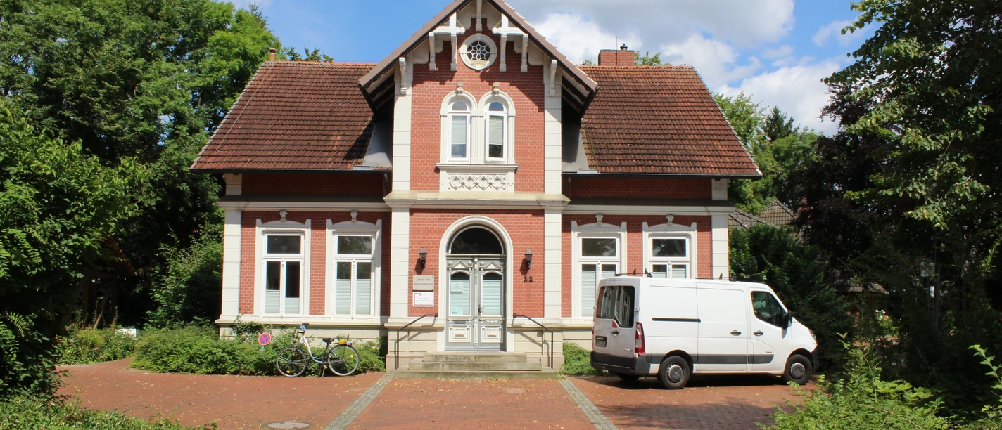 A red brick house with a gabled roof, two windows to the right and left of the door; white window frames.