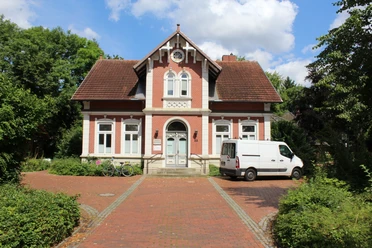 Martha Schuberth Haus Ein rotes Backsteinhaus mit Satteldach, zwei Fenstern rechts und links der Tür; weiße Fensterrahmen.