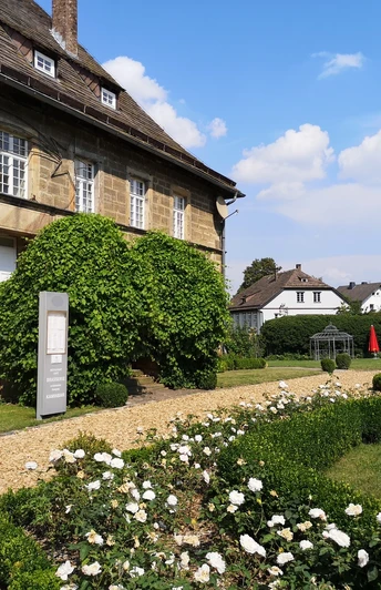 Schloss Gehrden Schloss Gehrden mit gepflegtem Rosengarten, historischem Sandsteinbau und klarer Himmel im Hintergrund.