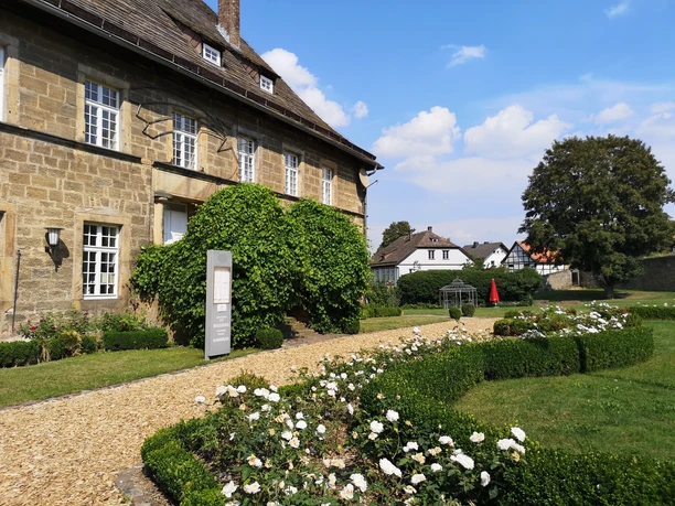 Schloss Gehrden Schloss Gehrden mit gepflegtem Rosengarten, historischem Sandsteinbau und klarer Himmel im Hintergrund.