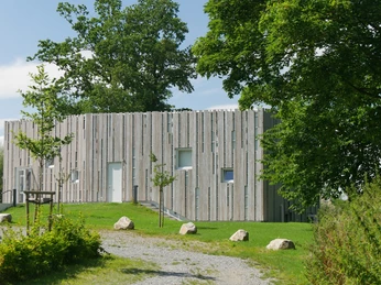 Besucherzentrum Marienmünster Besucherzentrum mit moderner Holzfassade, umgeben von grüner Wiese und Bäumen unter blauem Himmel.